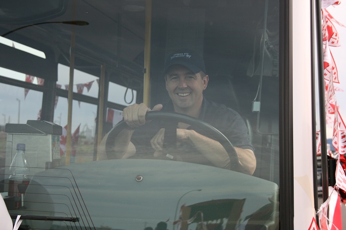 A transit driver sitting on a bus in the driver seat smiling at the camera