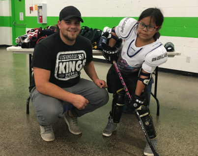 Child wearing hockey equipment with volunteer