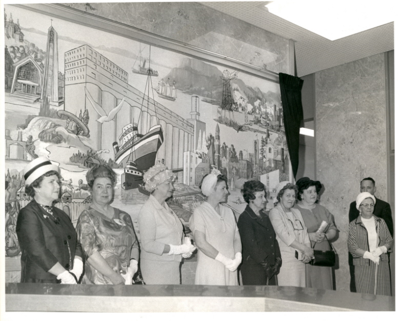 A group of people standing in front of a mural indoors wearing fancy attire