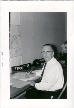 A man sitting at a desk wearing a white shirt and tie