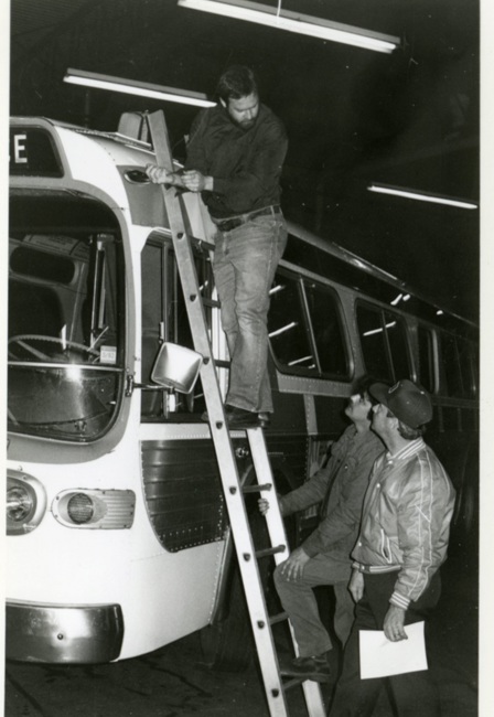 a person standing on a ladder that is leaning against a bus.