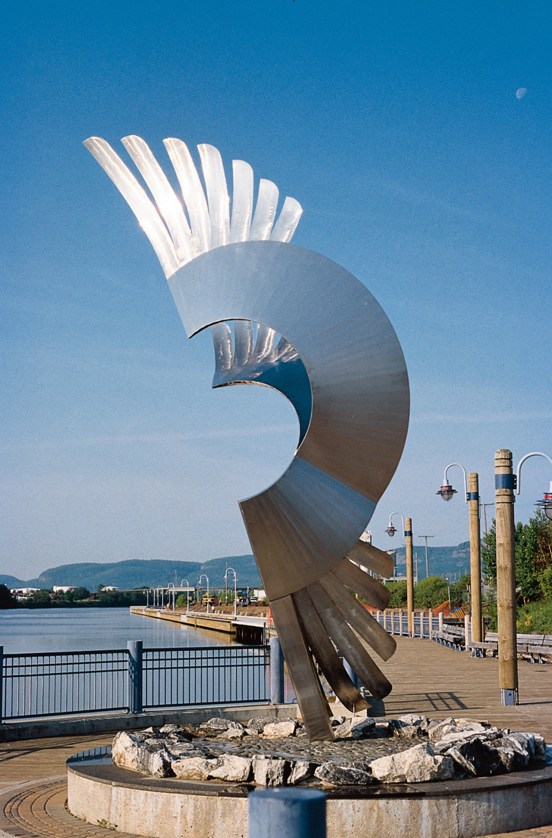 A metal sculpture in front of a blue sky with water behind