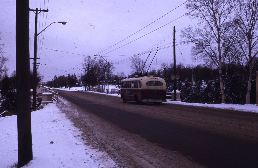 a trolley bus driving across a bridge on an unidentified street