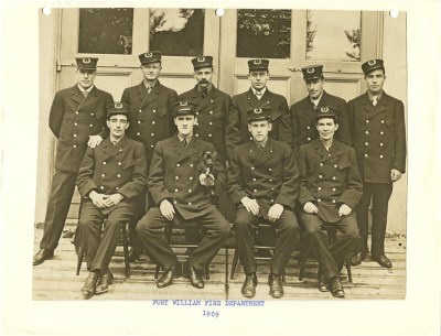 A group of firemen in uniform standing in front of glass doors