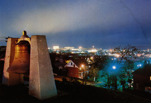 A bell hanging from a concrete structure overlooking the city