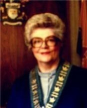 Mayor Dusty Miller sitting in a wood paneled room wearing large glasses and a large mayoral necklace