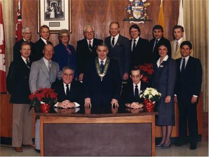 The 1986 City Council of Thunder Bay stand and sit together in an official portrait with the mayor in the centre