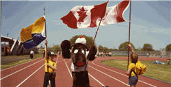 Two children holding flags with a person wearing a moose costume in between