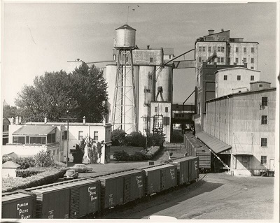 A black and white photo of a grain elevator with train cars in front