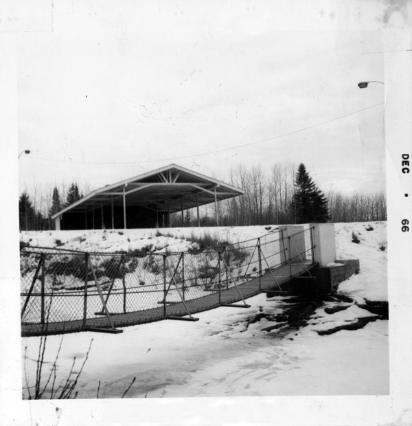 A wooden bridge crossing a creek with a building in back
