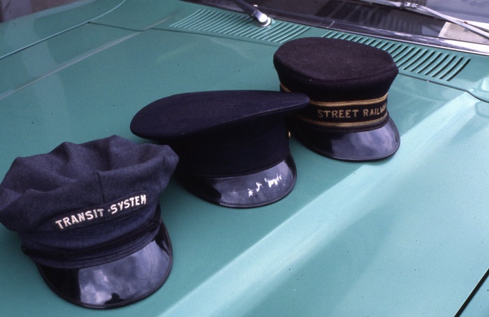 Three transit driver hats sitting on the hood of a teal car