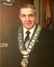 Mayor Jack Masters in a wood paneled room wearing robes and a large necklace