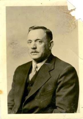 A man sits for an official portrait wearing a suit and tie